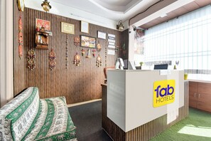 A reception area with a wooden panel wall, a reception desk, a couch, and a window with a view. - Fabhotel D7 (Jaipur)