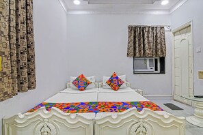 A bedroom with a bed, two pillows, a window with curtains, an air conditioning unit, and a door. - Fabhotel Wellesley (Kolkata)