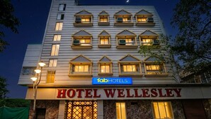 Ein mehrstöckiges Hotel mit einem auffälligen Schild über dem Eingang, auf dem 'HOTEL WELLESLEY' und 'fabHOTELS' steht.