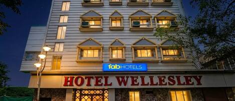 Un hotel de varios pisos con un letrero llamativo que dice 'HOTEL WELLESLEY' y 'fabHOTELS' sobre la entrada.