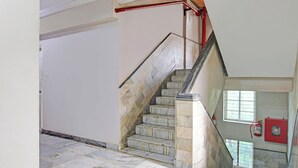 Eine Treppe mit Marmorstufen und Handlauf, die zu einer Zwischenebene führt, an der ein Feuerlöscher an der Wand angebracht ist.