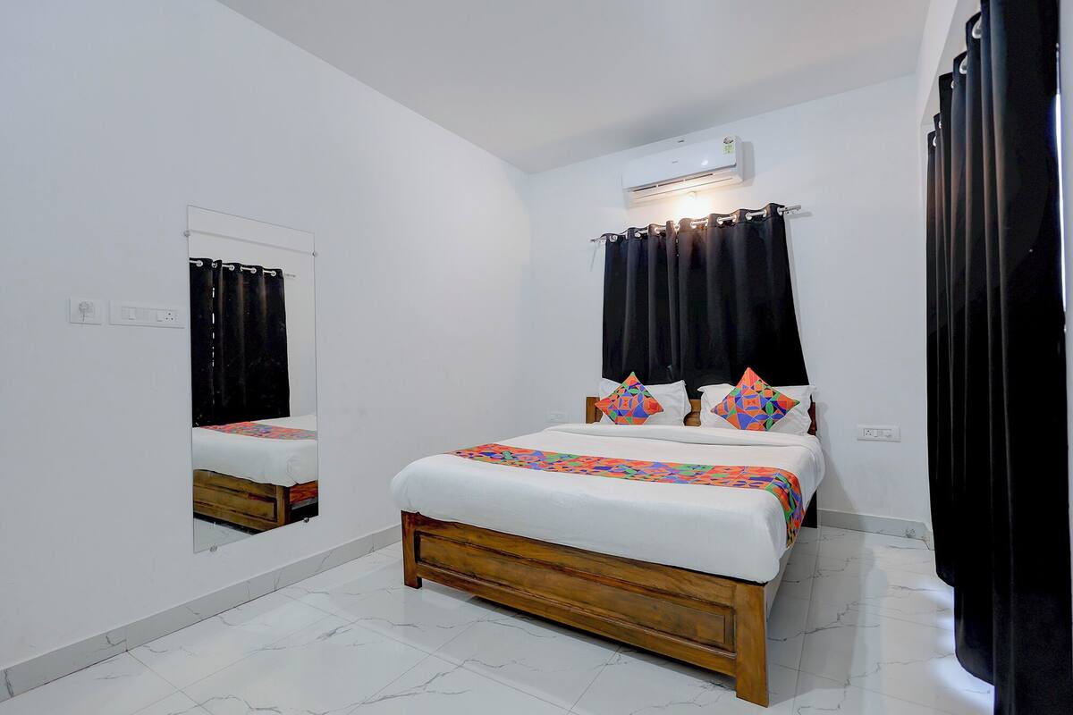 A bedroom with a bed, a mirror, an air conditioning unit, and a window with curtains.