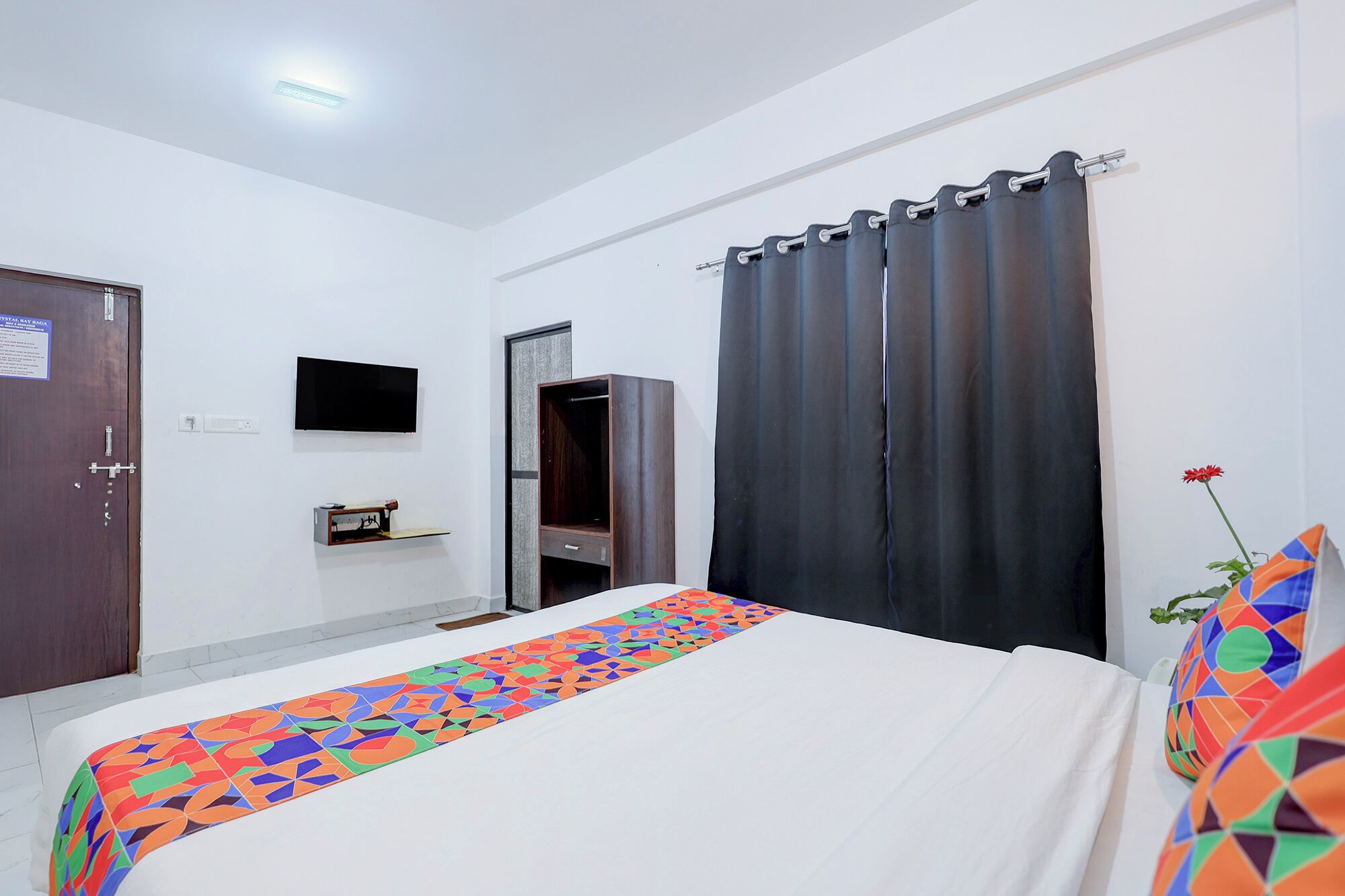 A hotel room with a bed, a TV, a wardrobe, and a curtain.