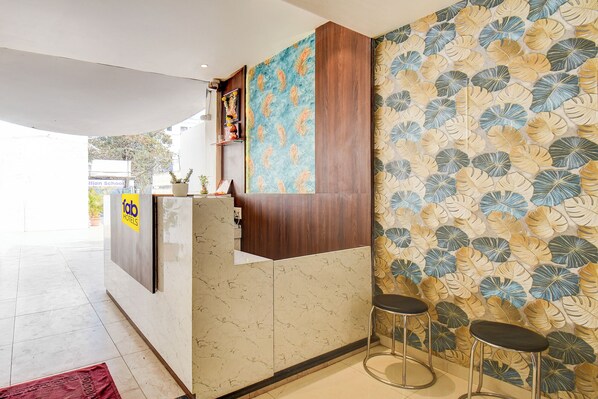 A hotel reception area with a marble counter, wooden paneling, and a wall with a leaf pattern. There are two bar stools and a potted plant on the counter. - Fabhotel Relax Inn Executive (Pune)