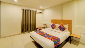 A hotel room with a large bed, a wooden headboard, a nightstand, a chair, and a window with curtains. - Fabhotel White Ridge Gachibowli (Hyderabad)