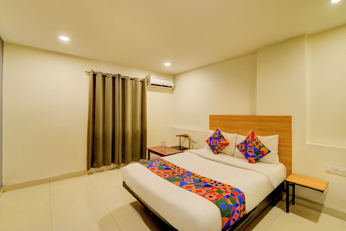 A hotel room with a large bed, a wooden headboard, a nightstand, a chair, and a window with curtains.