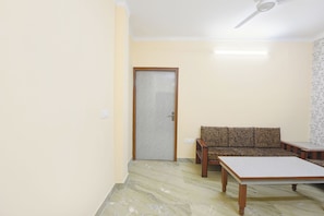 A room with a sofa, a table, a ceiling fan, and a door. - Fabhotel Zen Stay (New Delhi)