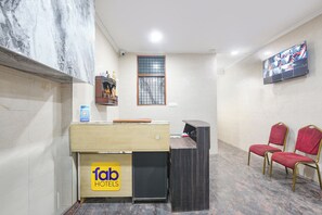 A hotel reception area with a counter, a TV mounted on the wall, and a seating area with chairs. - Fabhotel Zen Stay (New Delhi)
