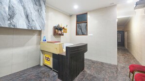 A hotel reception area with a marble wall, a reception desk, a small shelf with items, and a window with bars. - Fabhotel Zen Stay (New Delhi)