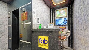 A reception area with a check-in/check-out sign, a digital display, and a bar area with a chair and a table. - Fabhotel Vishal Residency (Varanasi)