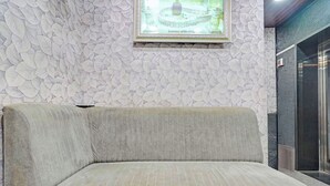 A corner sofa with a textured fabric, a framed artwork on the wall, and a dark-colored door to the right. - Fabhotel Vishal Residency (Varanasi)