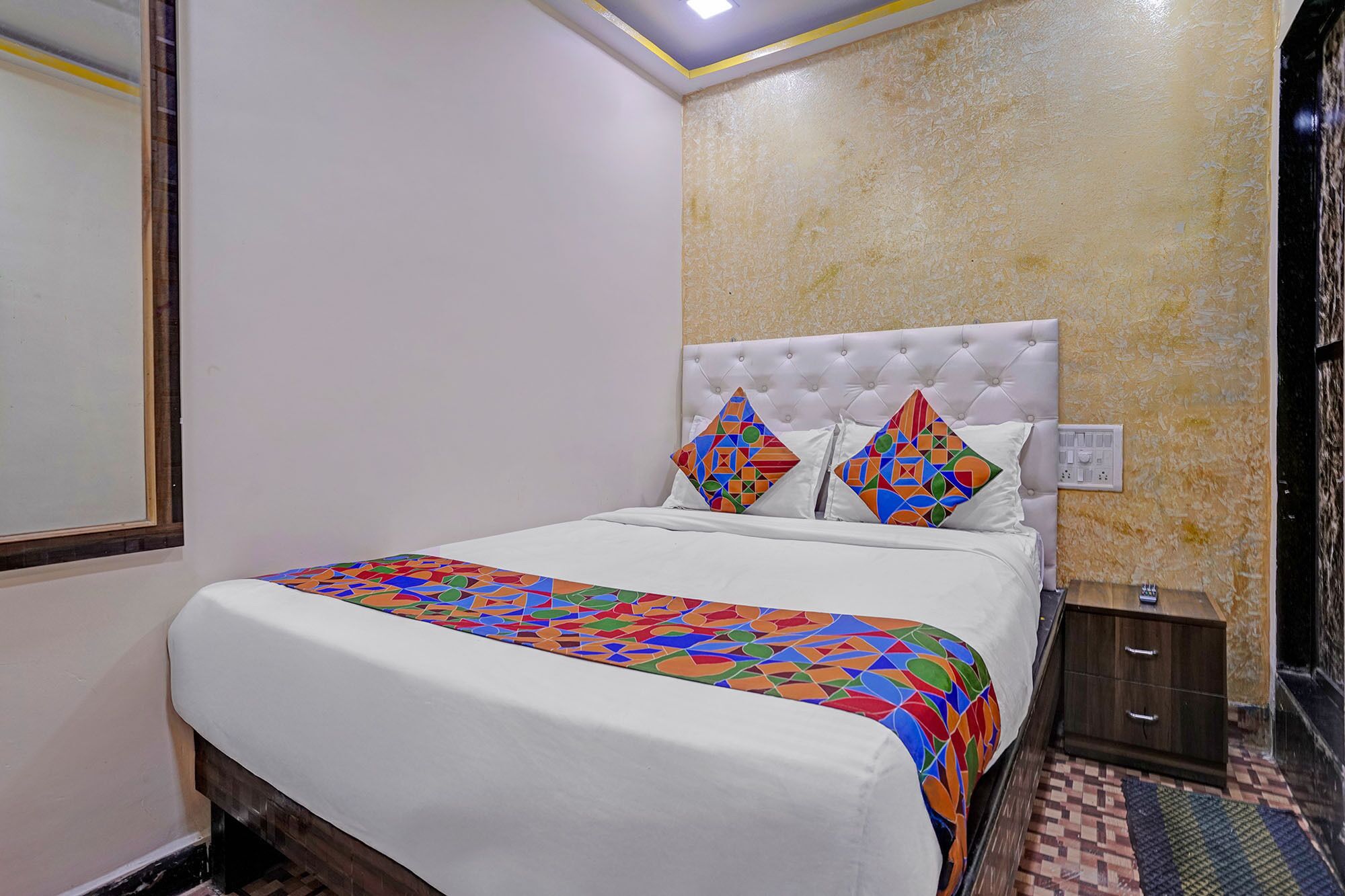 A hotel room with a bed, a nightstand, a mirror, and a textured wall.