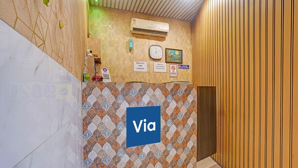 A hallway with a patterned wall, a clock, a 'Check Out' sign, and a 'Via' sign. - Fabhotel Om Residency (Mumbai)