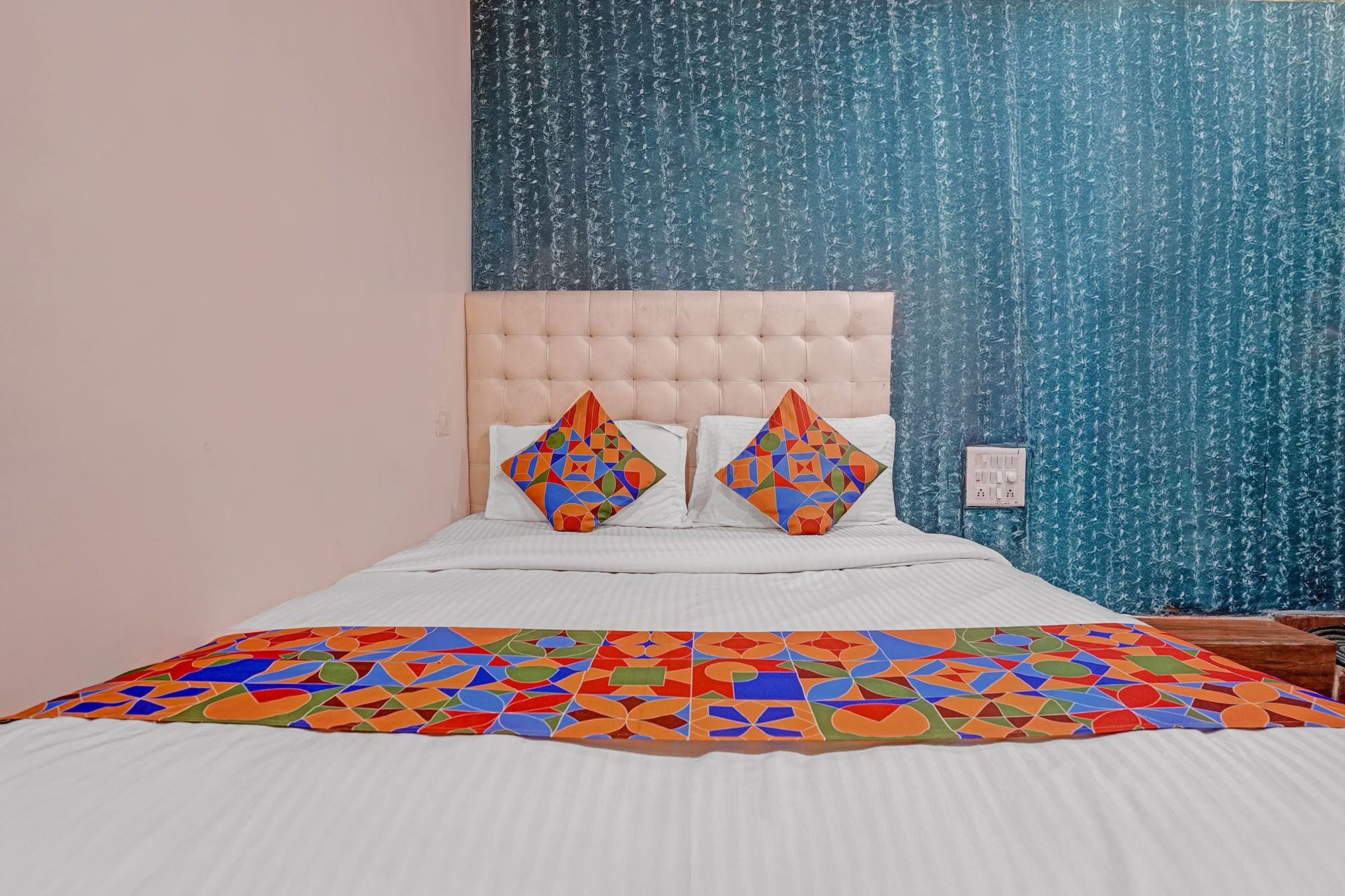 A bed with a white duvet, two pillows with geometric patterns, and a colorful geometric-patterned bedspread.