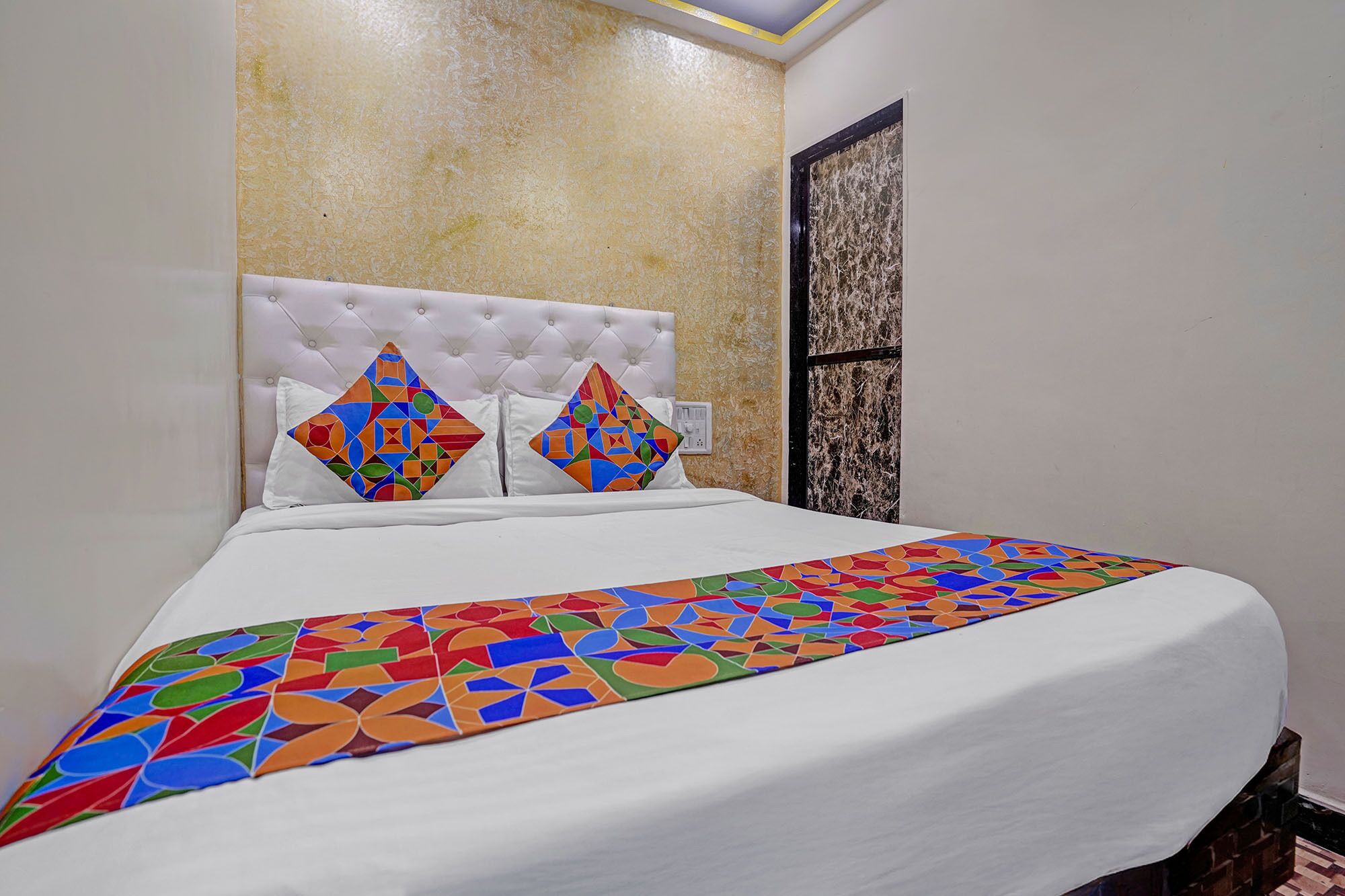 A bed with a white headboard and two pillows with colorful geometric patterns.