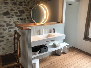 A bathroom with a stone wall, a wooden vanity with a mirror, a sink, and a bench. - House for rent in downtown Biarritz with a shaded terrace. (Biarritz)