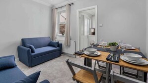A modern living room with a blue sofa, a dining table set for two, and a large mirror reflecting the room. - East Croydon Home, Near Station & Gatwick Airport (Greater London)