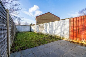 A fenced backyard with a grassy area, a brick wall, and a wooden fence.