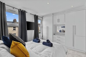 A modern bedroom with a large bed, white wardrobe, and a TV mounted on the wall.