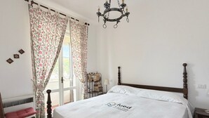Quarto com cama, cabeceira de madeira, lustre, janela com cortinas e mesa de cabeceira com abajur.