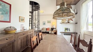 Uma área de refeições com uma mesa de madeira comprida, cadeiras, um lustre e uma escada.