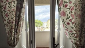 Uma janela com cortinas florais, vista para edifícios e uma varanda.
