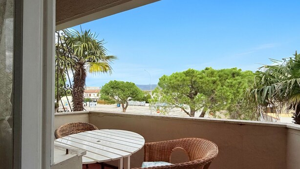 Uma varanda com móveis de vime, uma mesa branca e vista para árvores e edifícios.