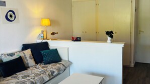 A small, well-lit room with a sofa, two white tables, a lamp, a fish decoration, a plant, and a wardrobe. - Apartment Arzon - 1 bedroom and terrace (Arzon)