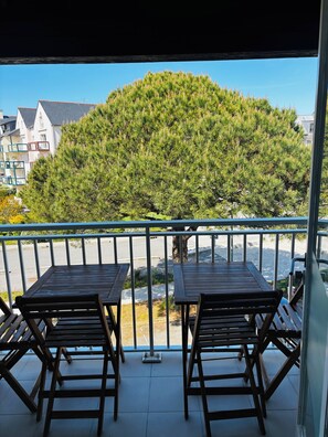 A balcony with two wooden tables and chairs, overlooking a tree and buildings. - Apartment Arzon - 1 bedroom and terrace (Arzon)