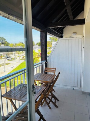 Ein Balkon mit Holztisch und -stühlen, einem weißen Tor und Blick auf eine Wohngegend.