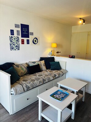 Ein Zimmer mit einer Couch, zwei weißen Tischen, einer Lampe und Wanddekorationen.