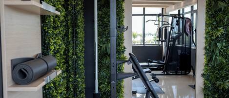 Un gimnasio con equipo de ejercicio, una banca y una pared cubierta de vegetación.