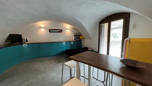 A compact kitchen with a curved counter, a dining table, and a window with blinds.