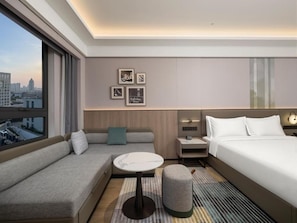 Habitación de hotel moderna con sofá, una mesita, cama, mesita de noche y vista a la ciudad.