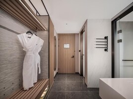Corredor moderno de hotel com um banco de madeira, um roupão pendurado na parede e uma porta com um aviso.