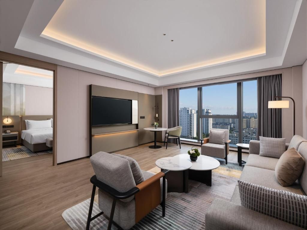 Habitación de hotel moderna con vistas a la ciudad, televisor de pantalla plana, sofá, mesa de centro y un pequeño comedor.