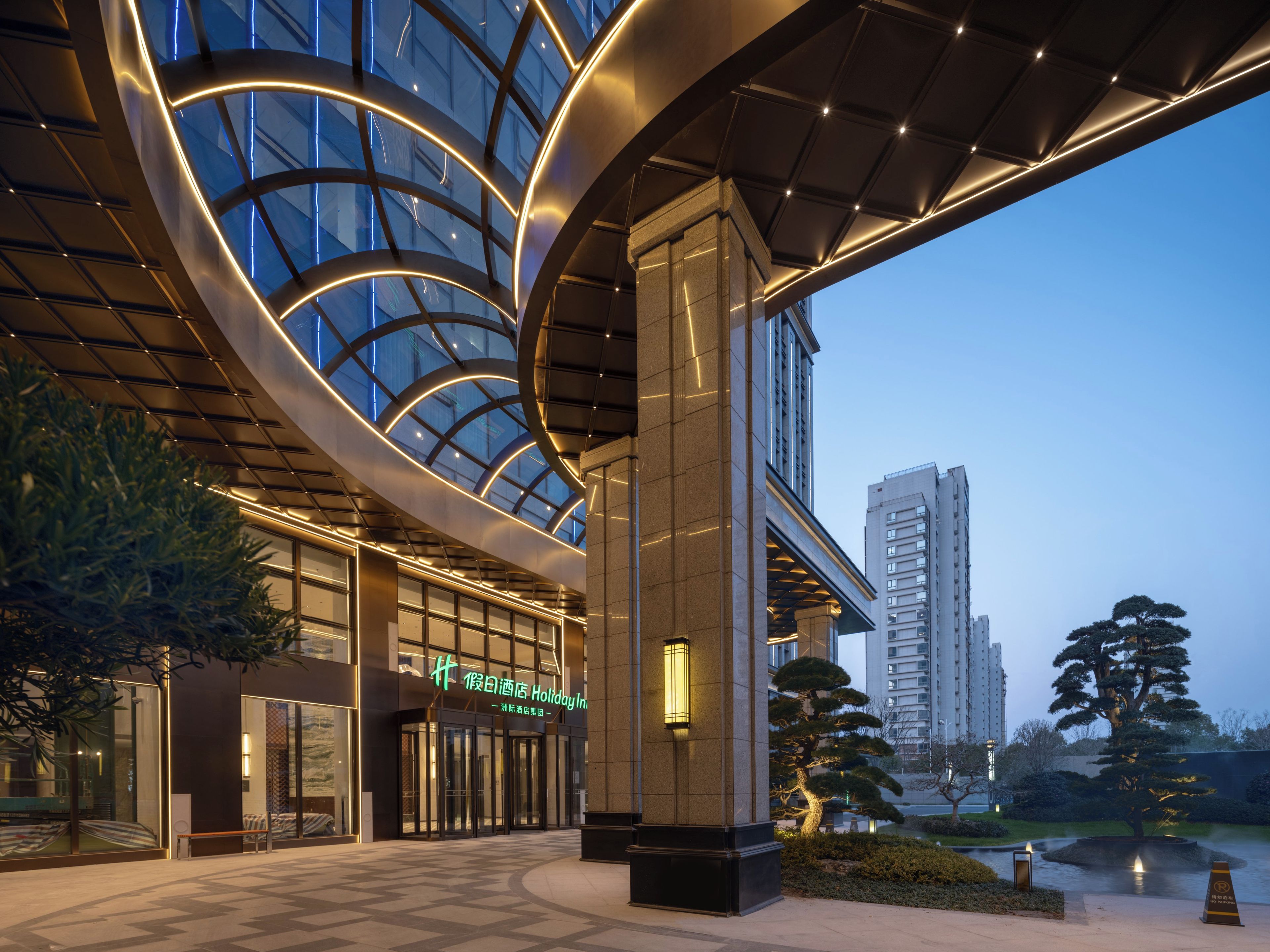 A hotel entrance with a modern design, featuring a curved glass facade and a prominent entrance with a sign.