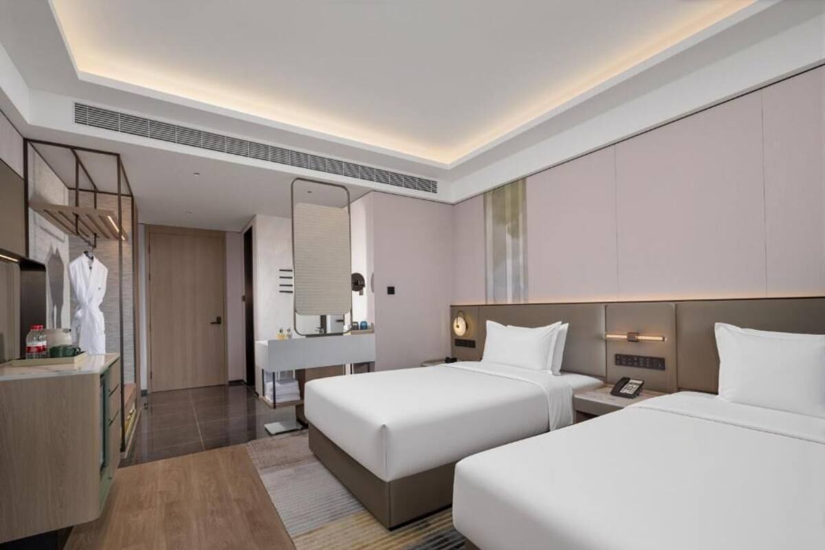 A hotel room with two beds, a bathroom, a vanity, and a mirror.