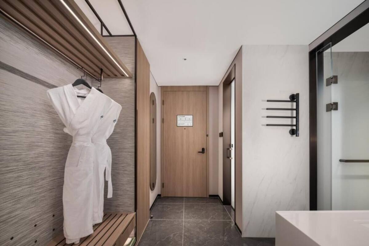 A modern hotel hallway with a wooden bench, a robe hanging on the wall, and a door with a sign.