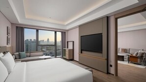 Ein modernes Hotelzimmer mit einem großen Bett, einem Flachbildfernseher, einer Couch und Blick auf die Stadt.