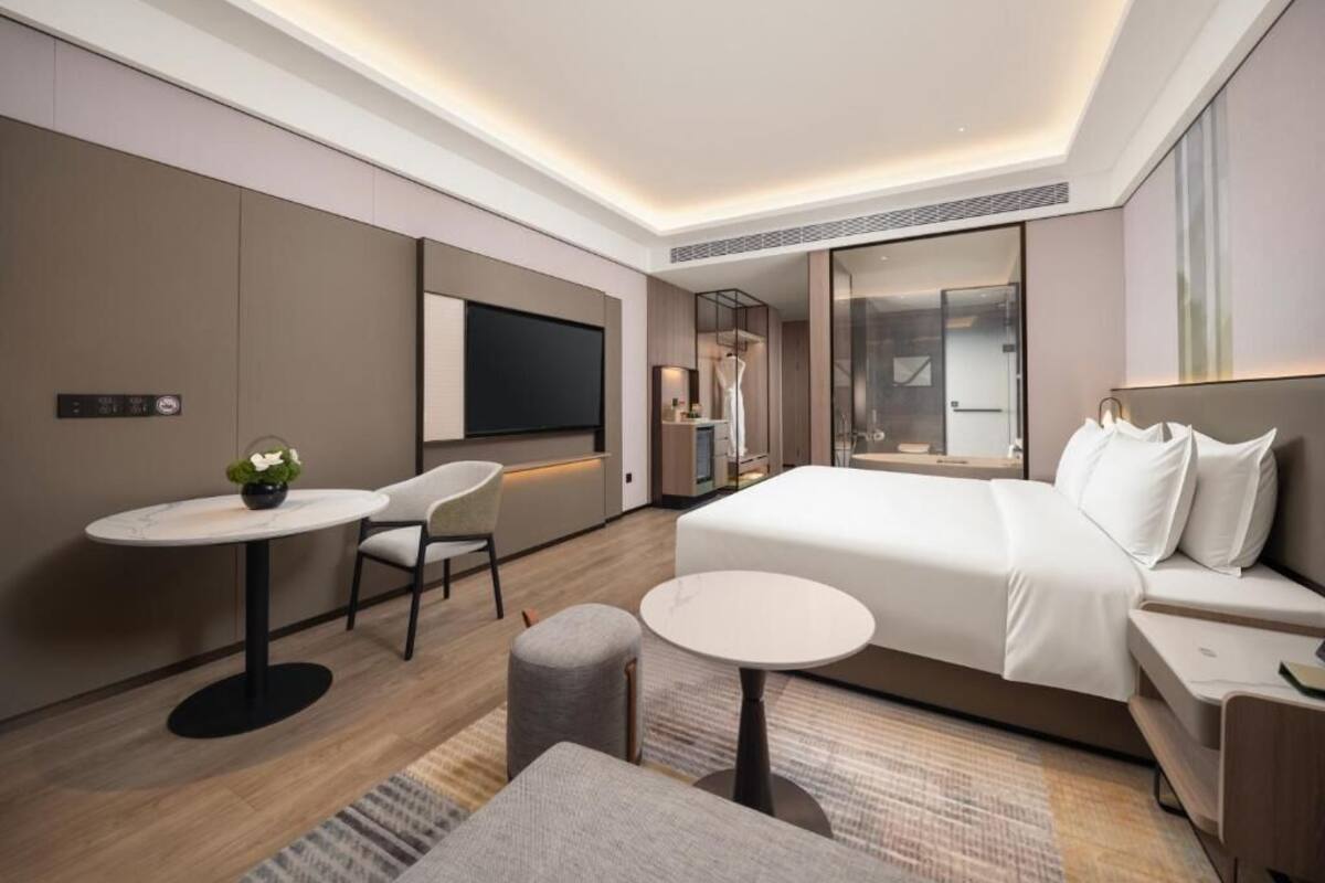 A modern hotel room with a large bed, a desk, a chair, and a TV.