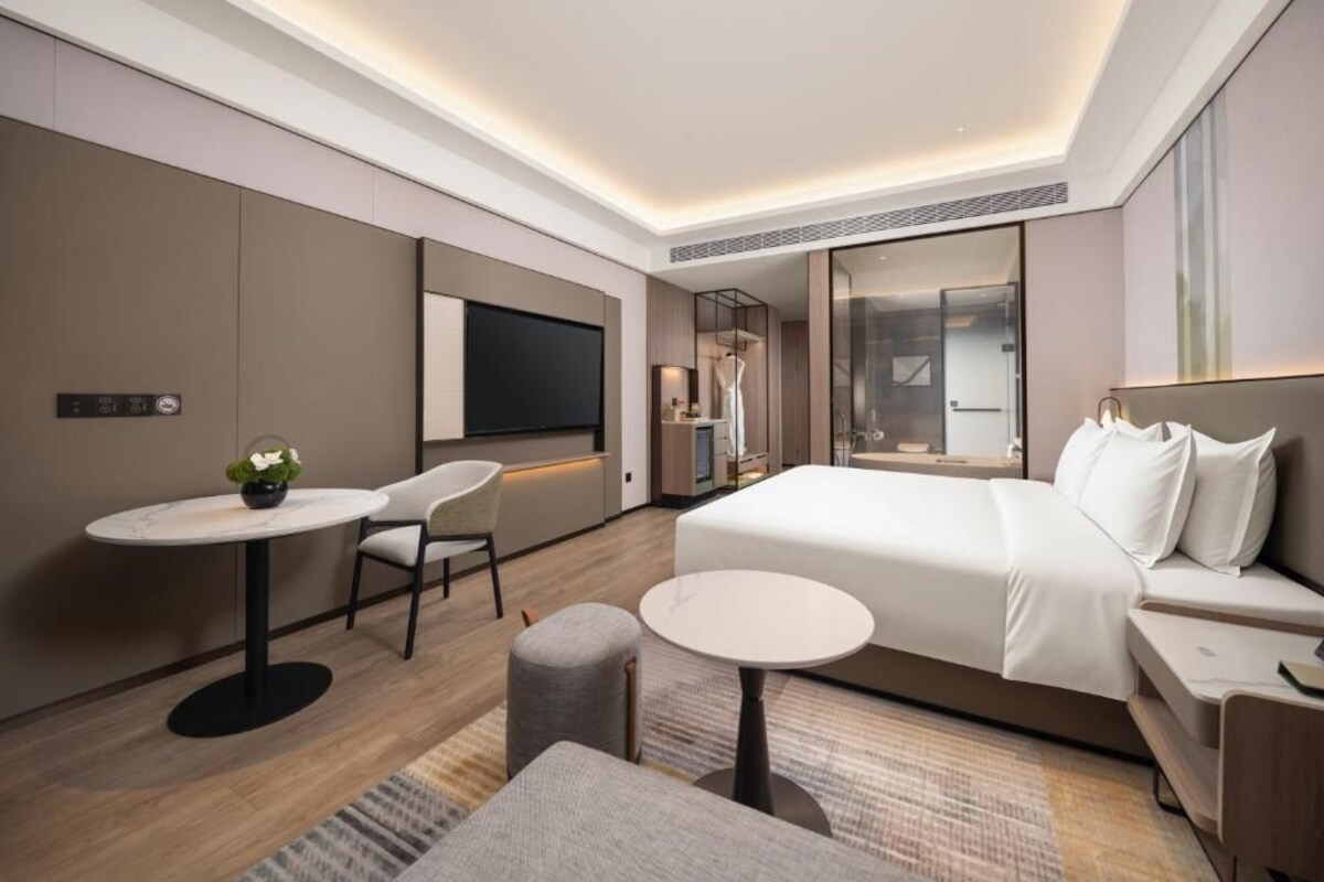 A modern hotel room with a large bed, a desk, a chair, and a TV.