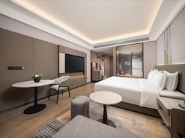 Quarto de hotel moderno com uma cama grande, uma escrivaninha, uma cadeira e uma televisão.