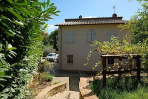 A two-story house with a tiled roof, a small garden, and a paved driveway.