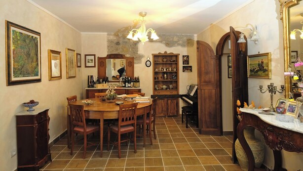 Une salle à manger avec une table en bois, des chaises, un lustre et un piano.