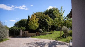 Une cour dallée de pierres, avec un mur en pierre, des arbres et un banc.