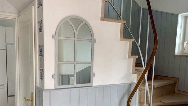 Una scala con ringhiera in legno e un muro bianco con una finestra.