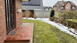 Una casa in mattoni con una porta nera, un piccolo giardino anteriore con ingresso piastrellato e un edificio moderno adiacente.