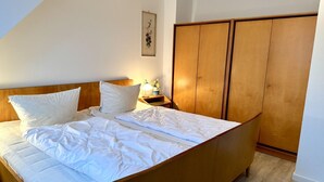 Camera da letto con un letto, un'armadietto in legno, un comodino, una lampada e un quadro appeso al muro.