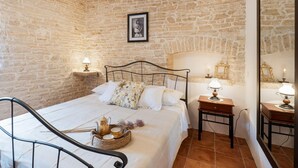 Ein Schlafzimmer mit Steinwand, einem Bett mit weißer Bettwäsche, zwei Nachttischen mit Lampen und einem gerahmten Bild an der Wand.